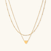 Delicate double-chain gold necklace with tiny heart pendant on cream background