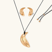 Gold-toned crescent moon pendant with textured surface on black adjustable cord, displayed with matching crescent earrings