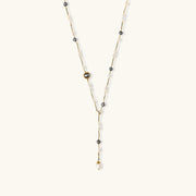 Y-shaped gold-plated necklace with white and gray freshwater pearls on cream background, showing adjustable drop design.